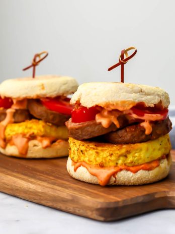 Two vegan tofu breakfast sandwiches on English muffins with vegan breakfast sausage.