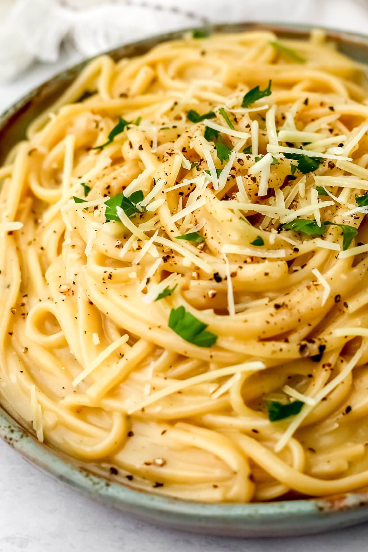 A close up of a creamy vegan cacio d pepe on a green plate.