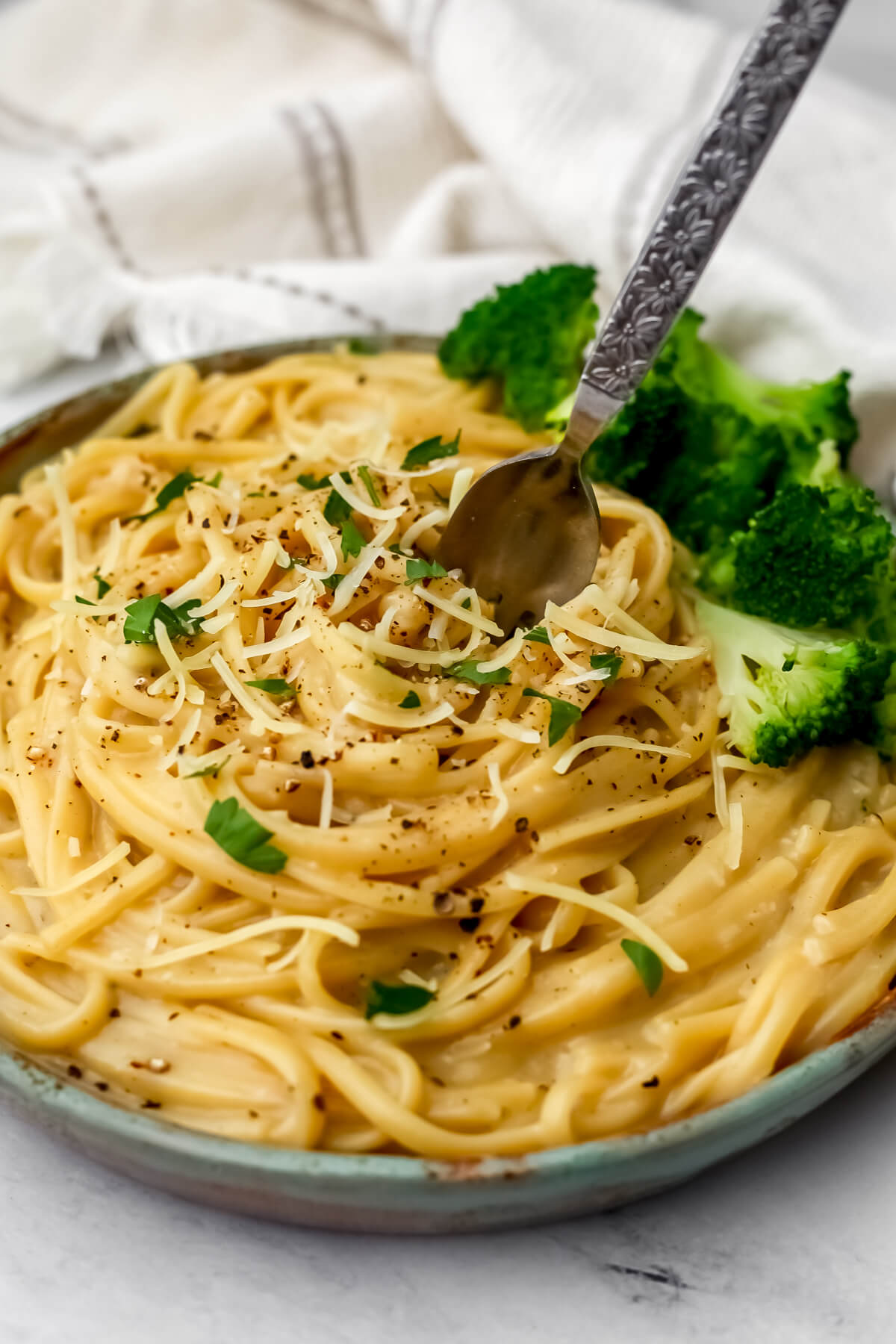 A plate of vegan cacio e pepe with a side of broccoli.