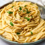 Vegan cacio e pepe on a green plate with a fork on the side.