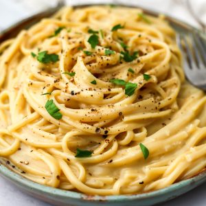 Vegan cacio e pepe on a green plate with a fork on the side.