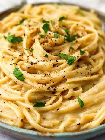 Vegan cacio e pepe on a green plate with a fork on the side.