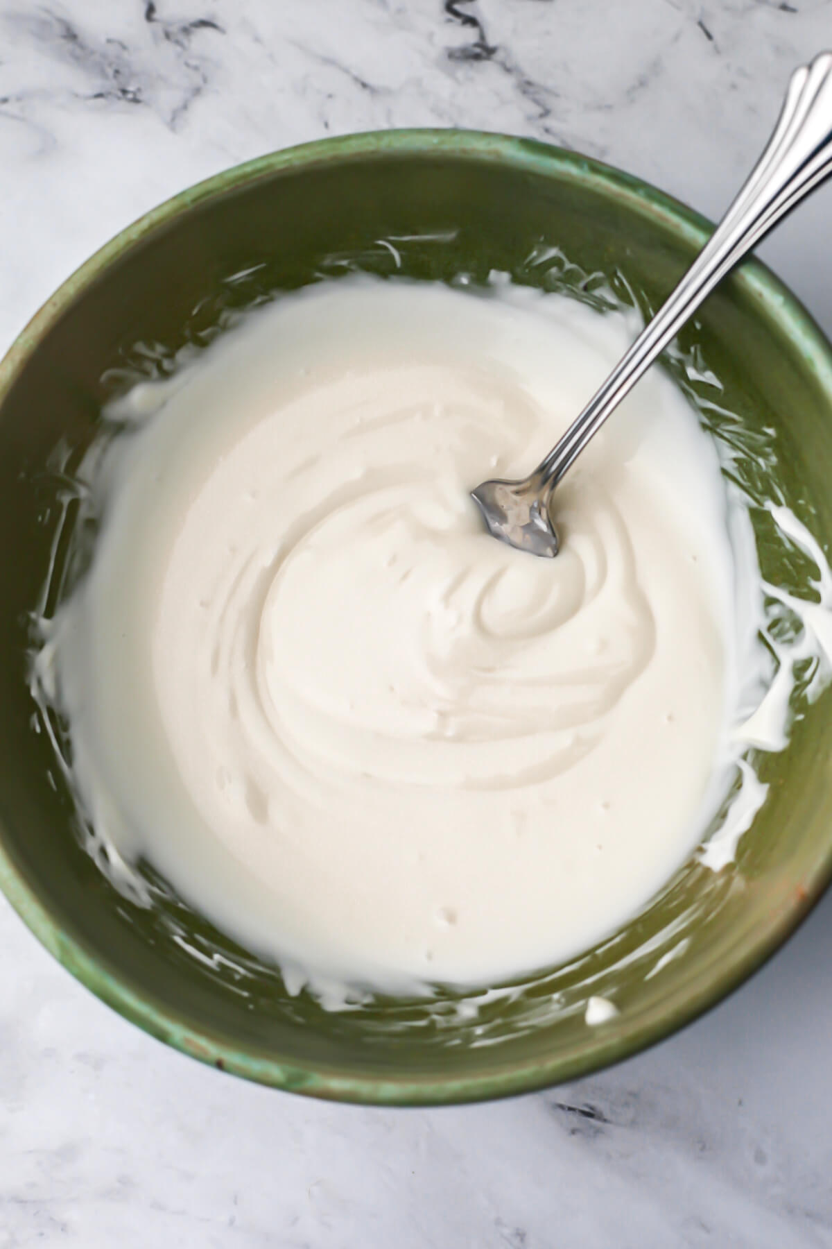A green bowl with vegan white chocolate chips melted and stirred together.