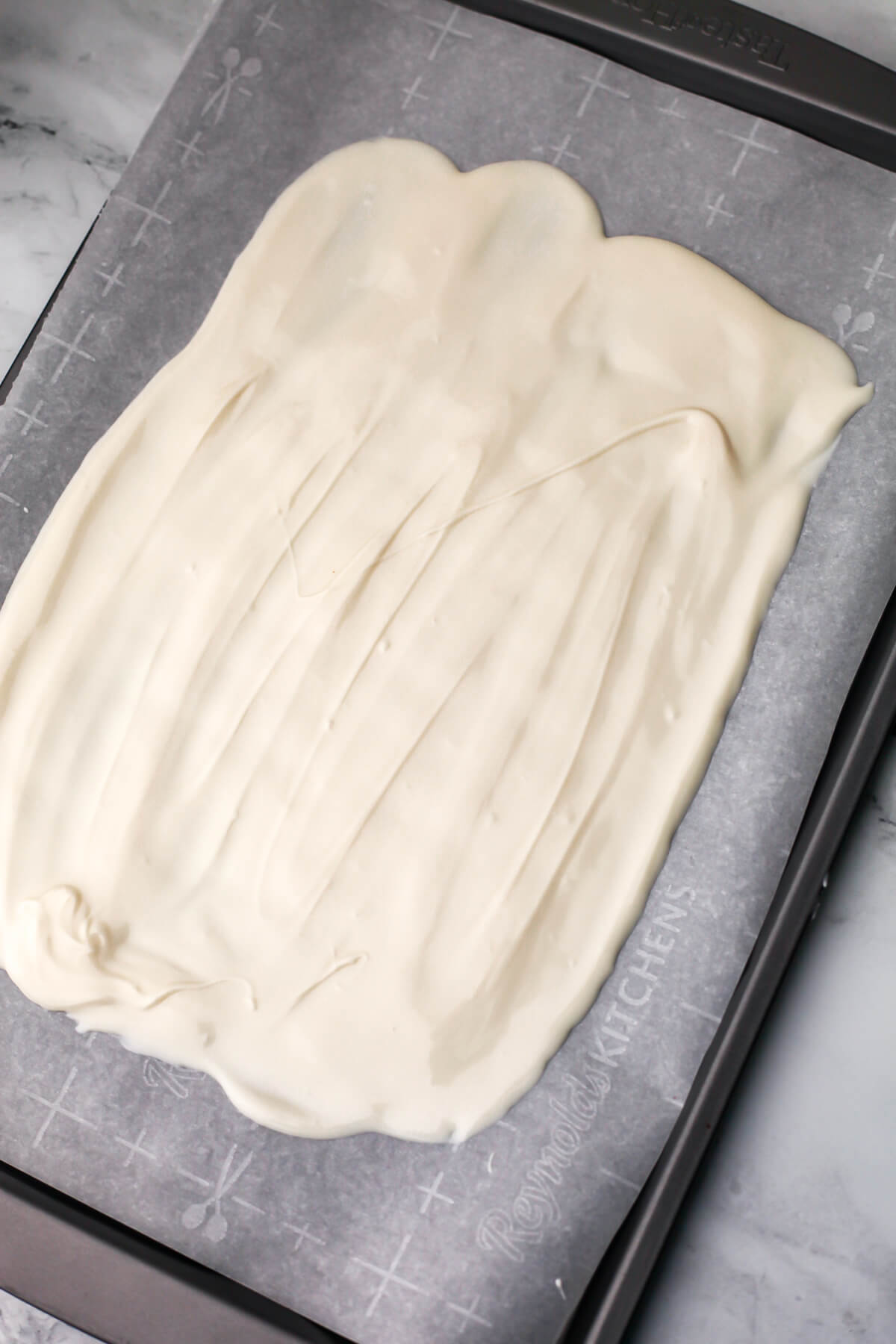 Melted white chocolate spread out on a piece of parchment paper.