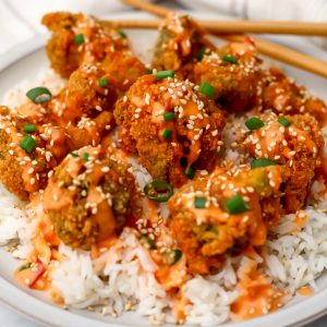 A plate of vegan bang bang broccoli served over white rice with chopsticks on the side.