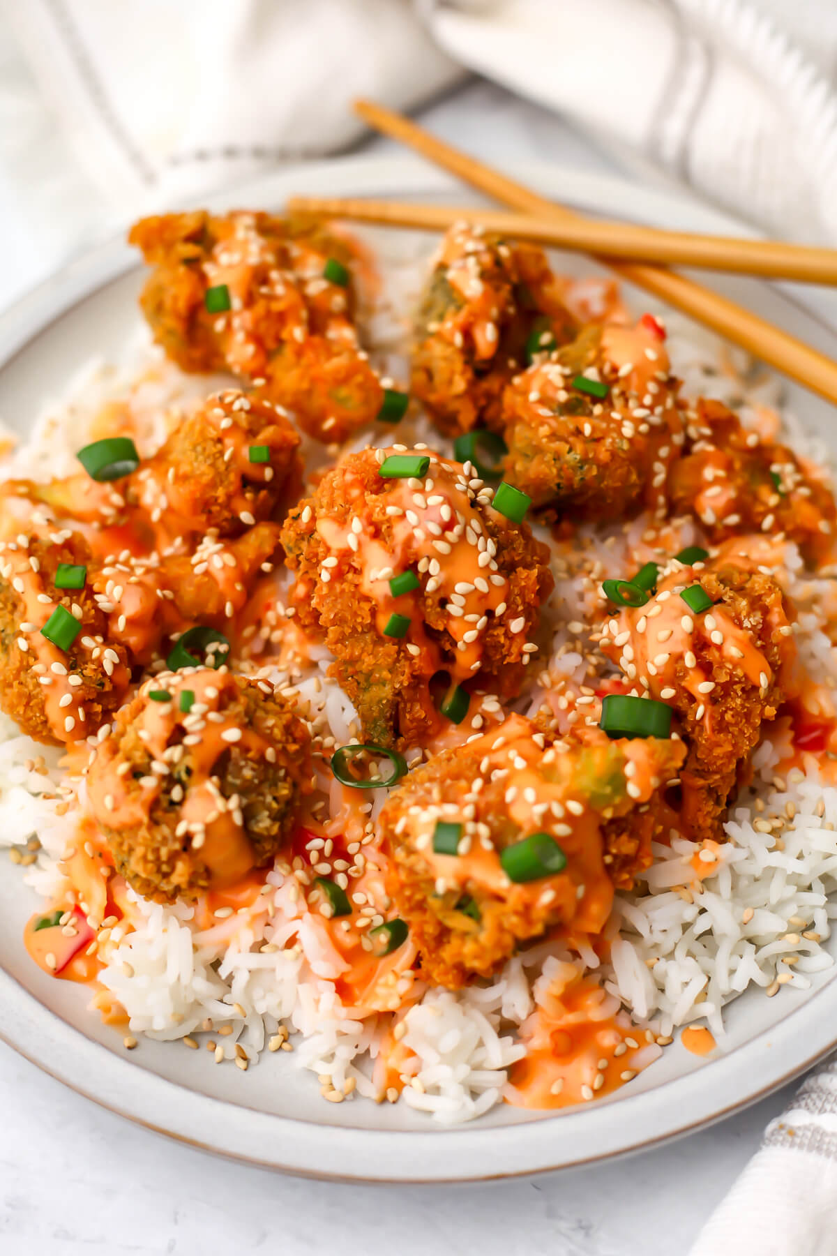 A top view of a plate filled with white rice with bang bang broccoli garnished with sesame seeds and green onions.
