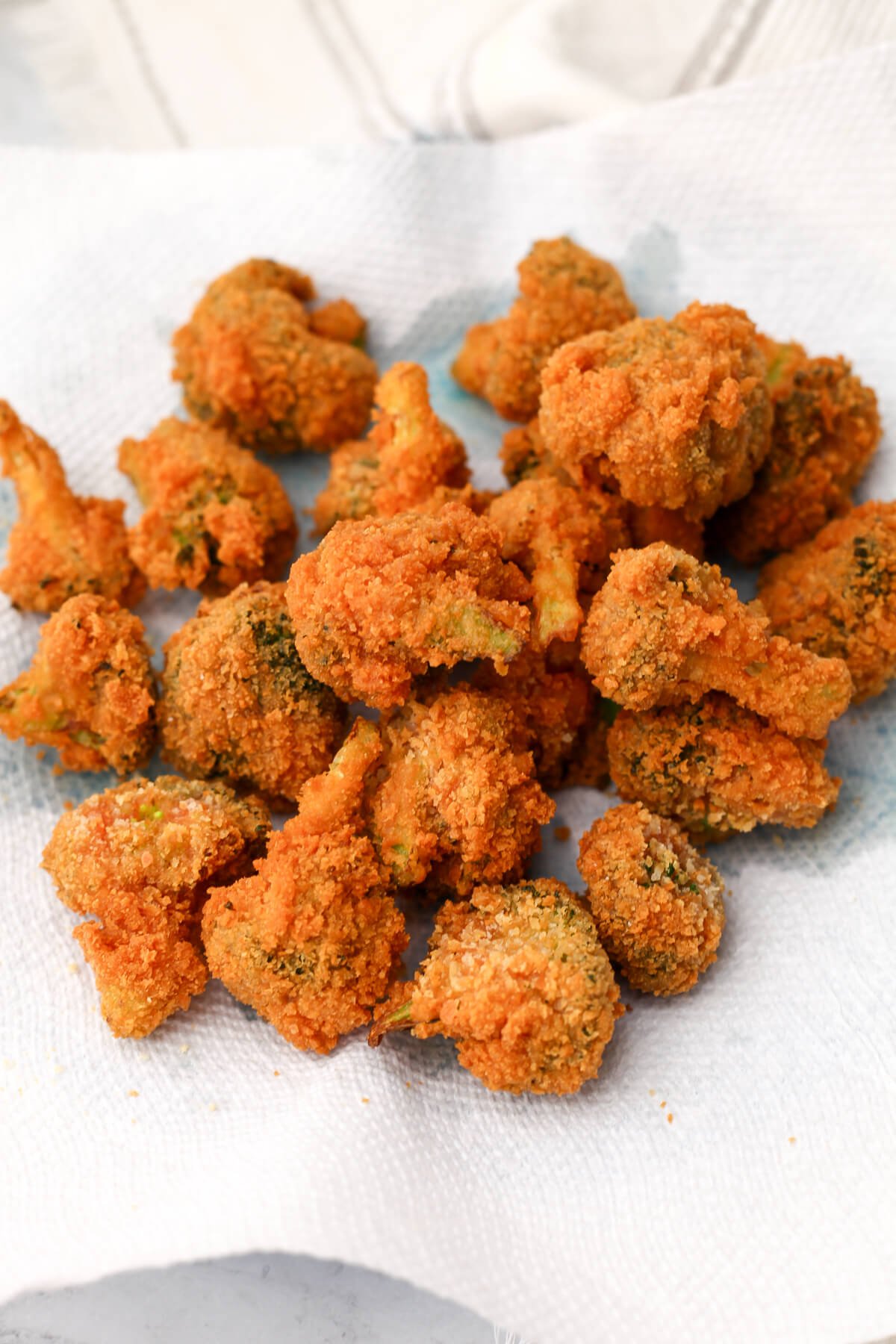 Fried battered broccoli on a paper towel after it has been fried.