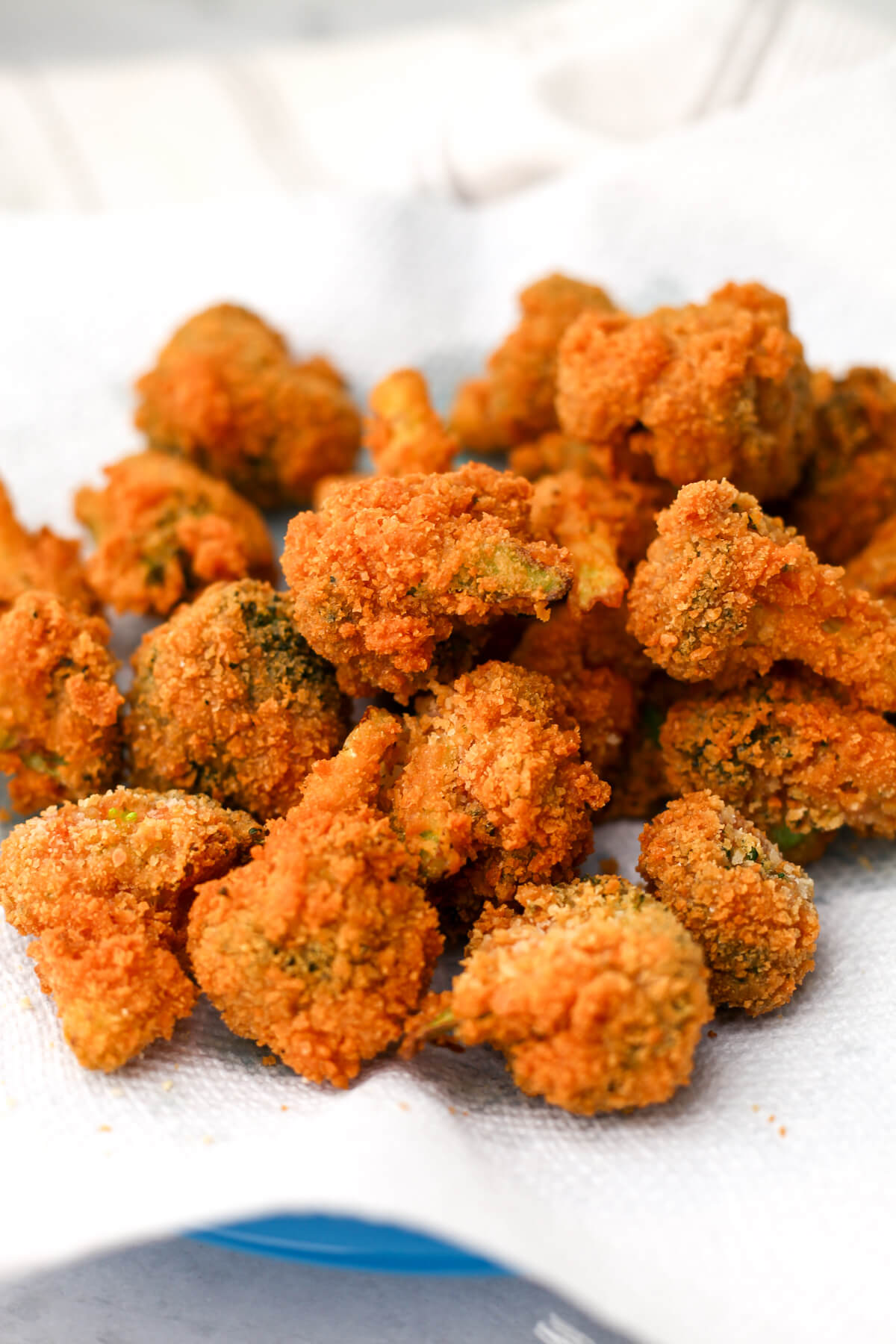 A pile of deep fried battered broccoli on a paper towel on a plate.