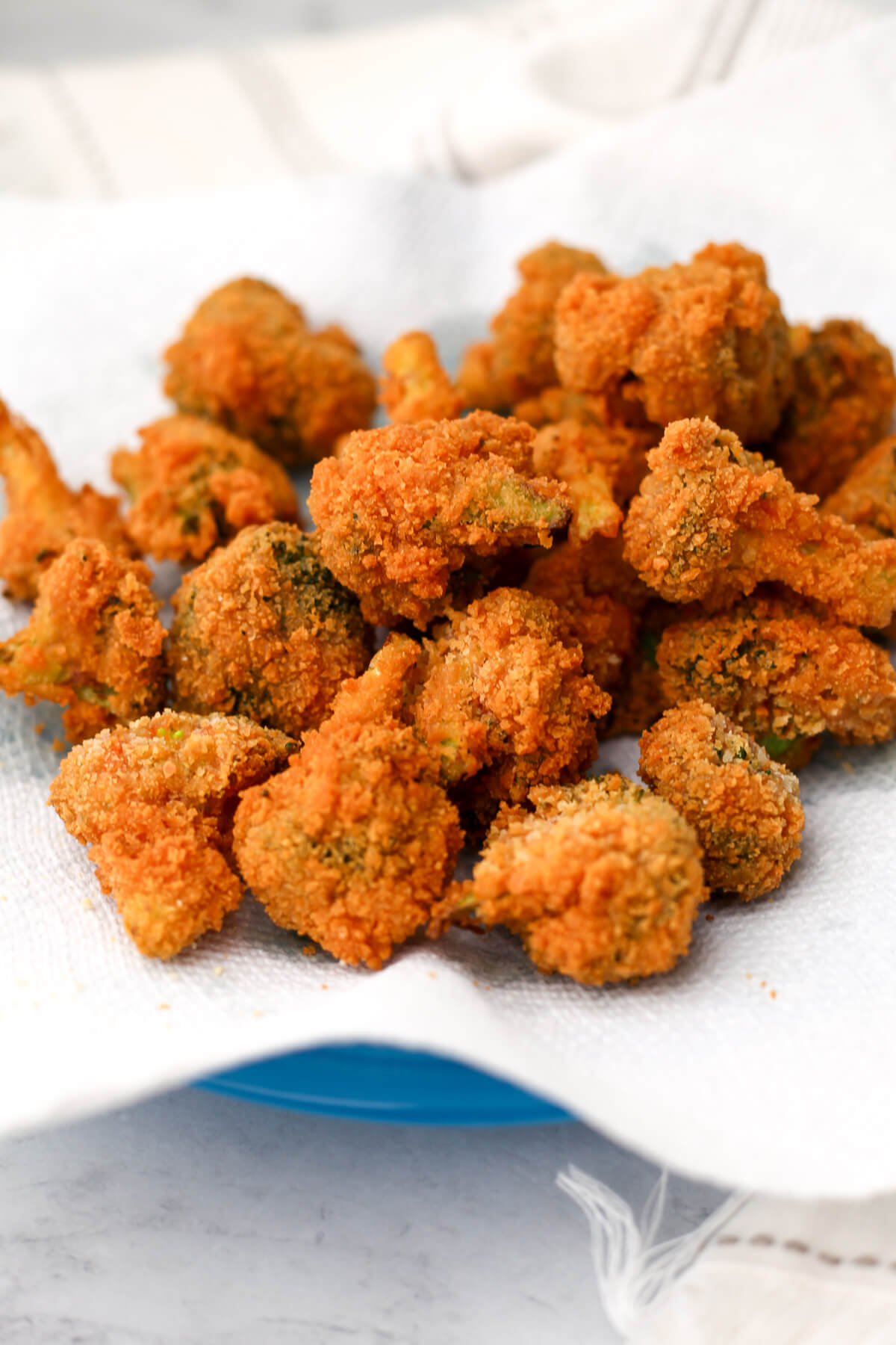 A plate full of golden brown vegan deep-fried broccoli on a paper towel.