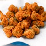 A blue plate with a paper towel on top filled with golden brown deep fried broccoli.