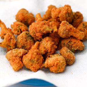 A blue plate with a paper towel on top filled with golden brown deep fried broccoli.