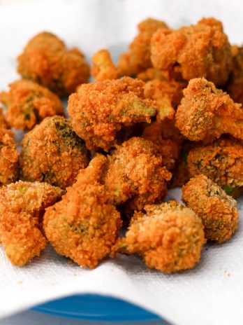 A blue plate with a paper towel on top filled with golden brown deep fried broccoli.