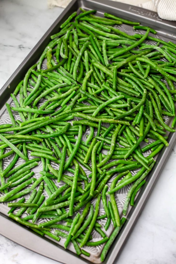 Frozen green beans drizzled with olive oil on a sheet pan before baking.