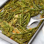 Roasted green beans from frozen on a sheet pan being scooped up with a metal spatula.