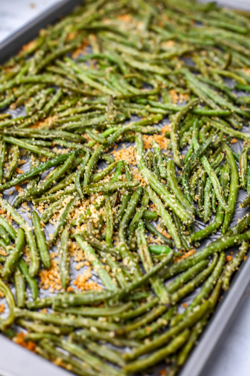 A close up of a sheet pan full of roasted frozen green beans tossed with garlic breadcrumbs.