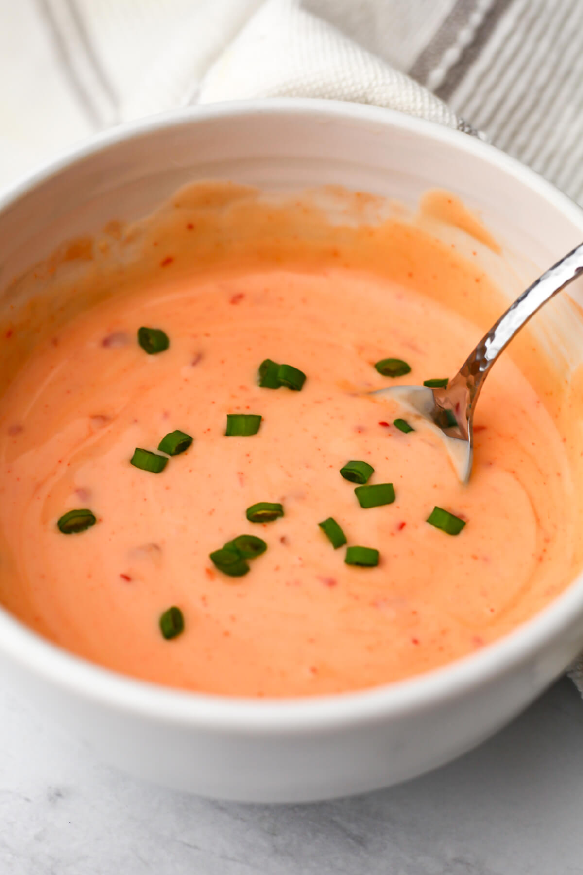A white bowl filled with vegan bang bang sauce topped with some green onions.
