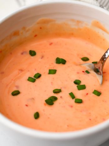 A white bowl filled with vegan bang bang sauce is being stirred with a spoon.