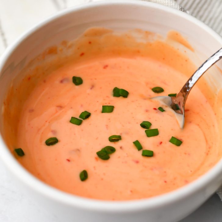 A white bowl filled with vegan bang bang sauce is being stirred with a spoon.
