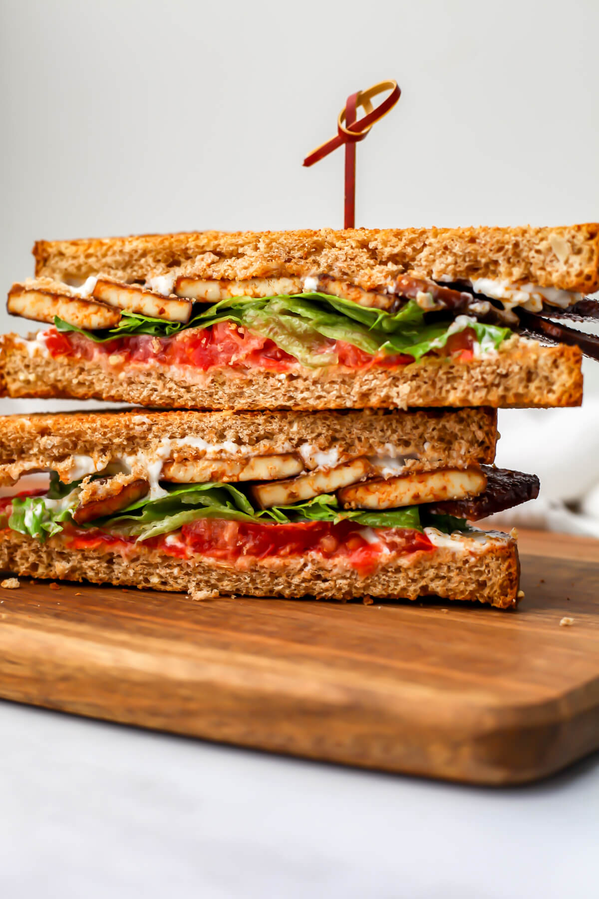 A tofu BLT sandwich sliced and stacked on a wooden cutting board.