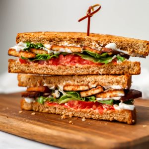 A Tofu BLT cut in half on a wooden cutting board.
