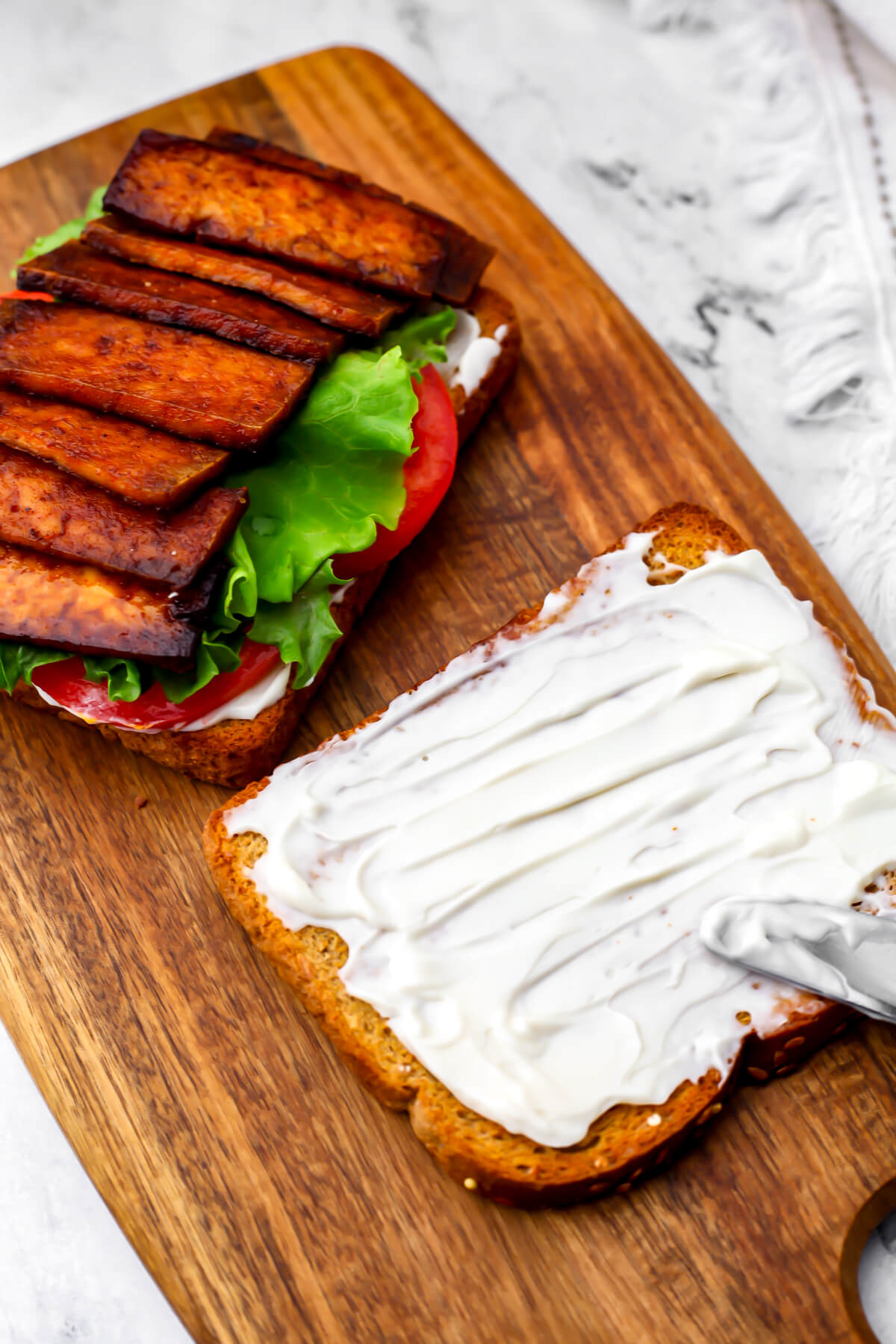 A tofu BLT being assembled on a wooden cutting board.