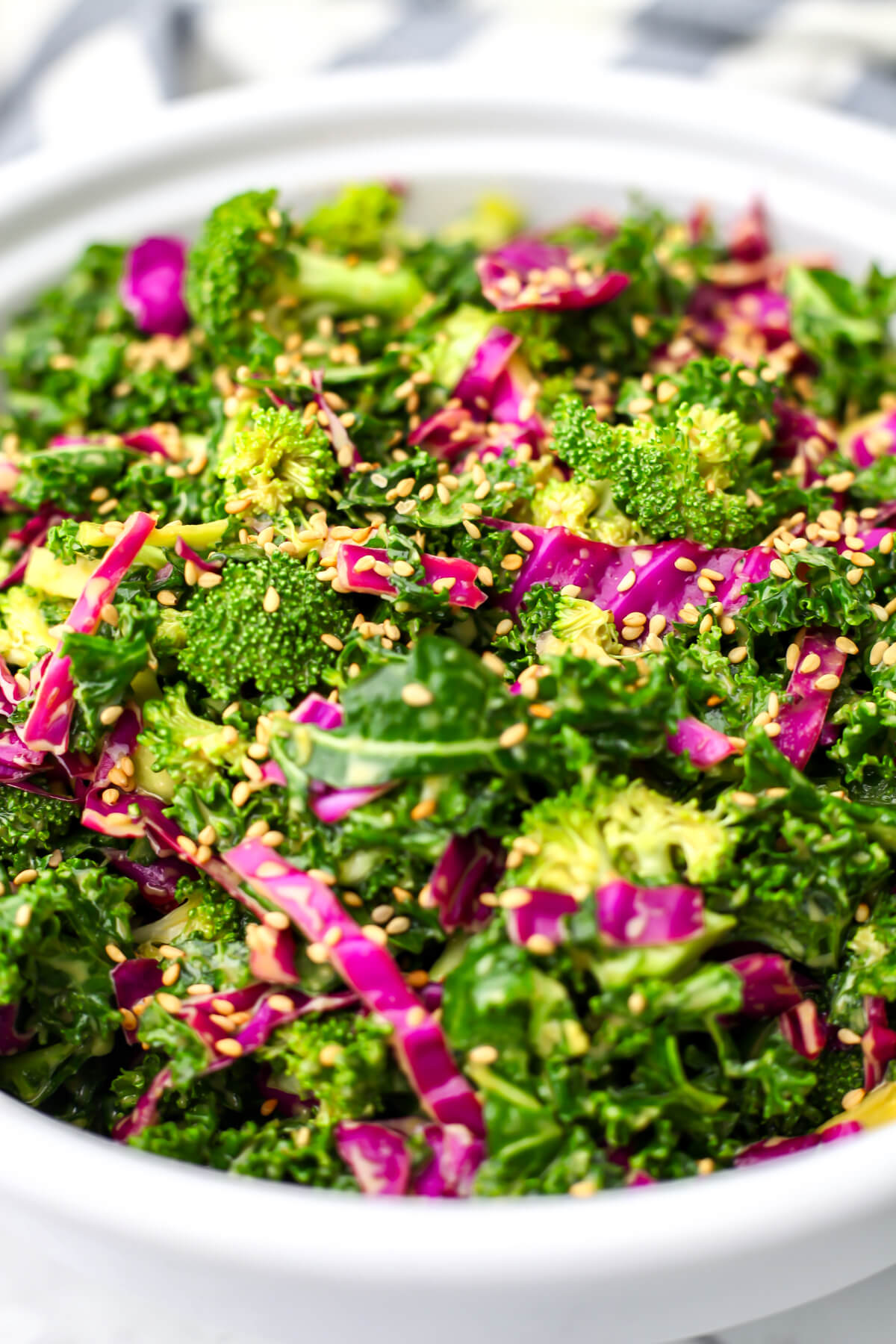 A large white salad bowl filled with crunchy kale salad with nutritional yeast dressing.