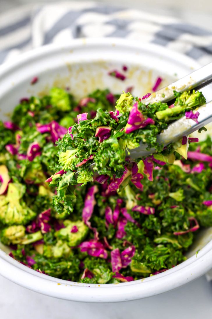 Crunchy kale salad being mixed with the dressing with tongs.