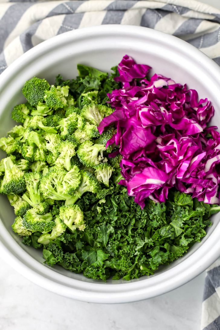A top view of kale, broccoli and purple cabbage in a white salad bowl.