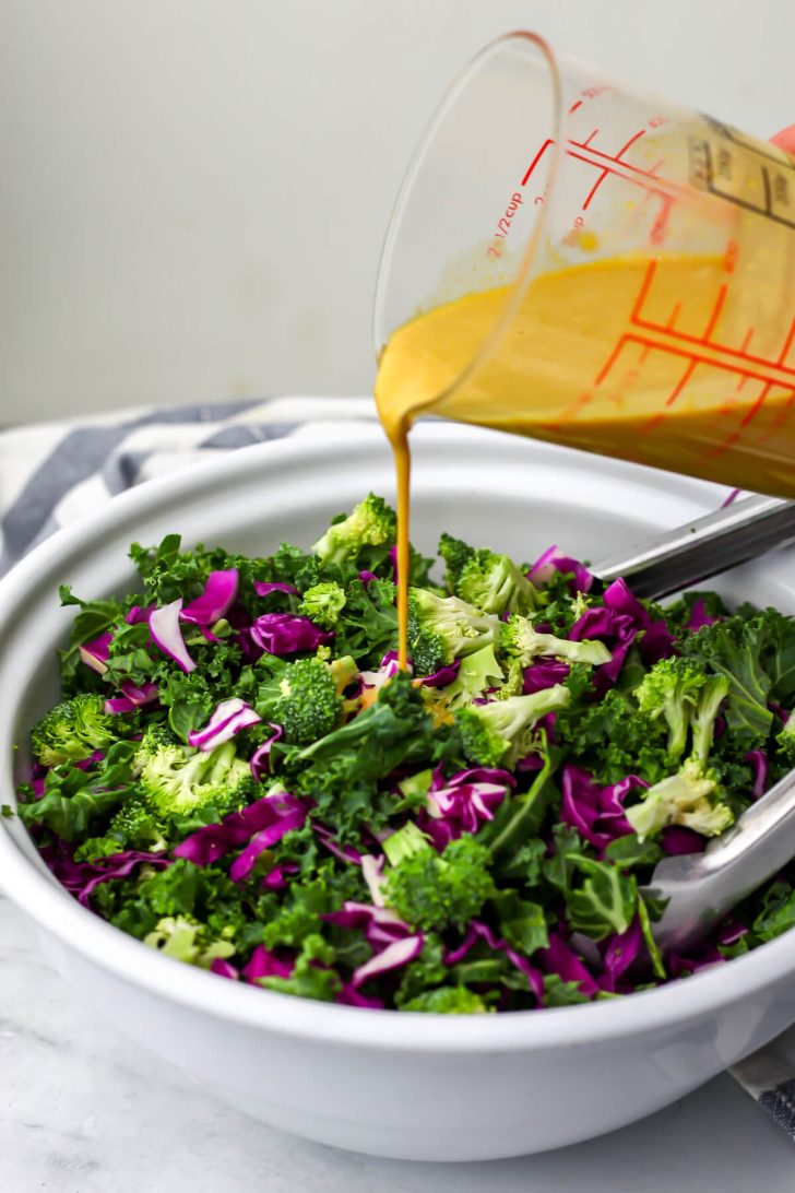Pouring nutritional yeast dressing over a kale salad.
