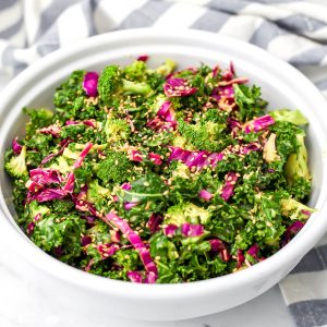 A white salad bowl filled with vegan crunchy kale salad with nutritional yeast dressing.