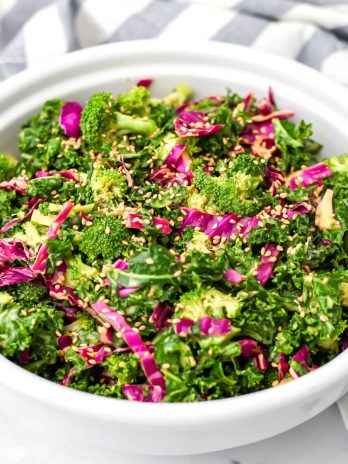 A white salad bowl filled with vegan crunchy kale salad with nutritional yeast dressing.