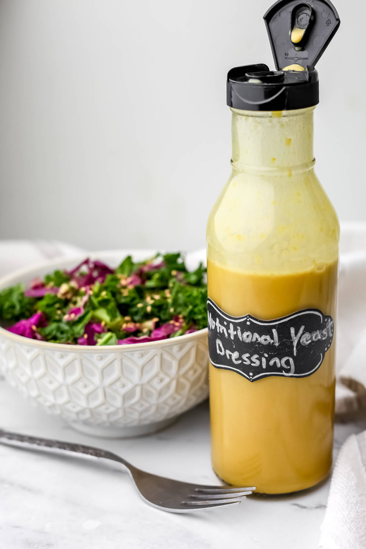 Nutritional yeast dressing in a glass bottle next to a kale salad.