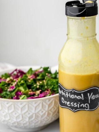 A glass bottle filled with nutritional yeast dressing sitting next to a kale salad.