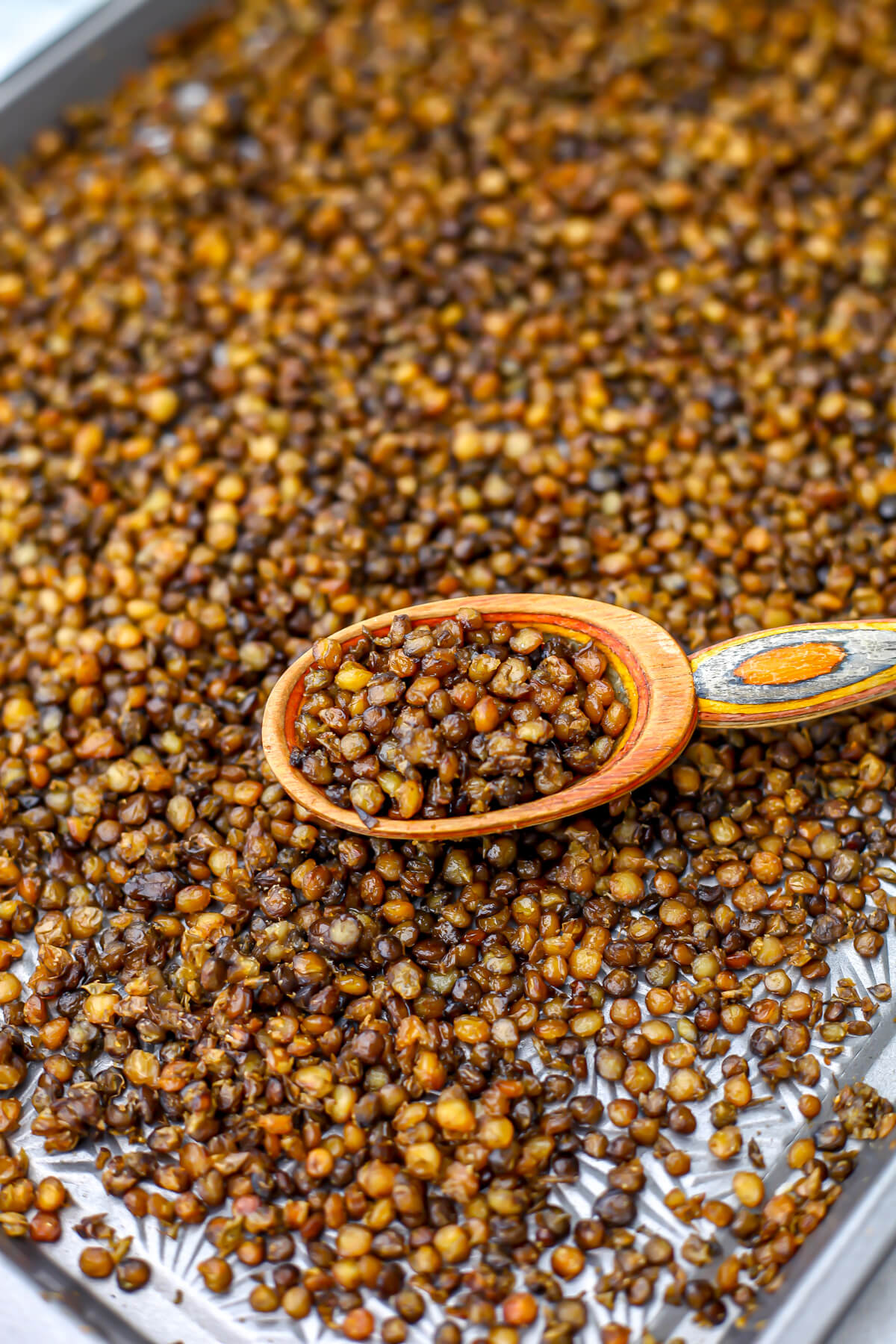 A sheet pan full of roasted lentils being scooped up with a wooden spoon.