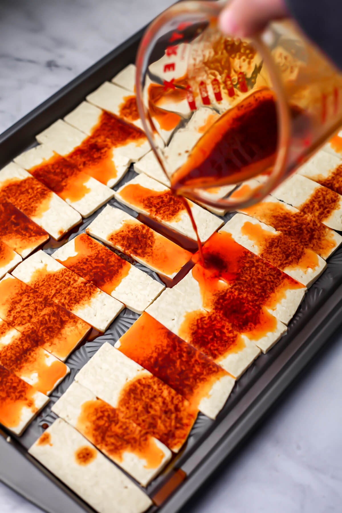 Pouring the smoky marinaded over the sliced tofu.