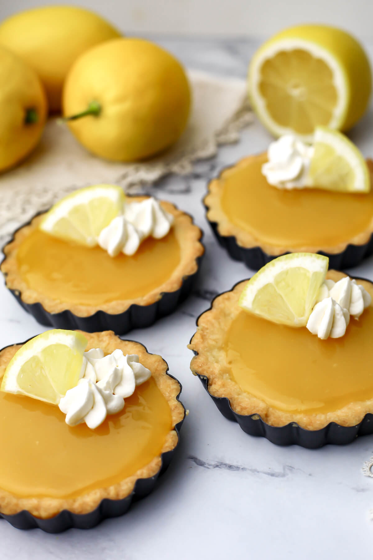 A side view of four vegan  lemon tarts with whipped cream and lemon slices on top.