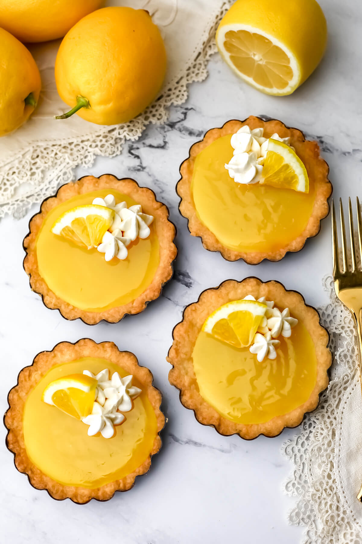 Four vegan lemon tarts with fresh lemons on the side.