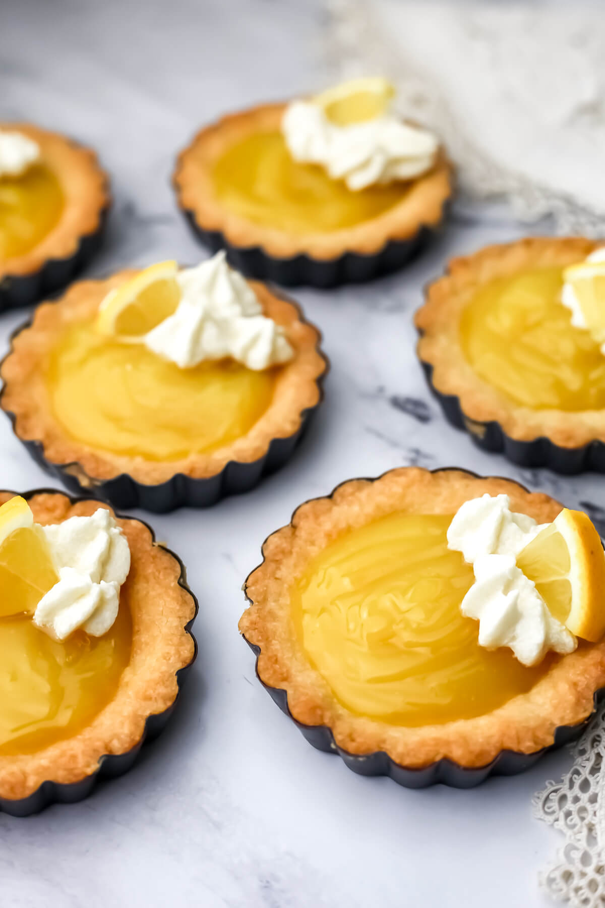 Six vegan lemon tarts on a marble countertop.