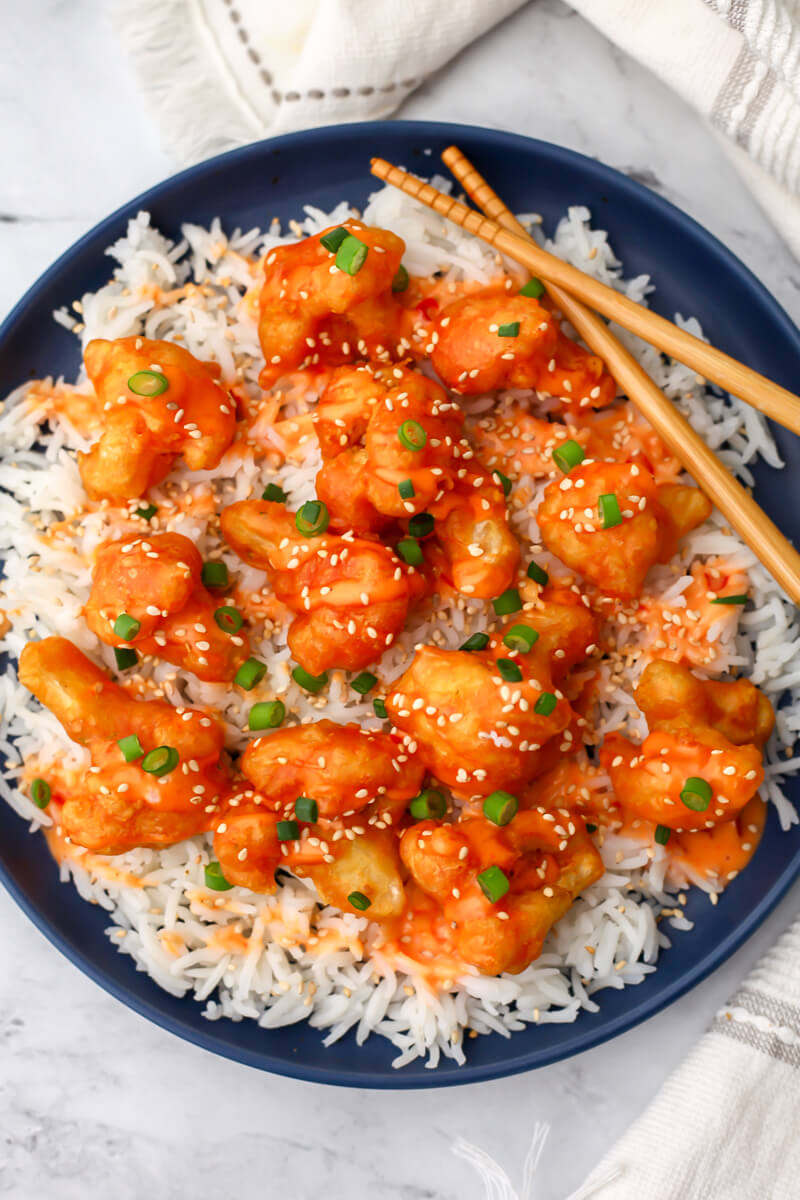 A top view of a plate of vegan bang bang cauliflower served over white rice with green onions and sesame seeds.