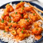 A close-up of a plate full of white rice with bang bang cauliflower served over it.