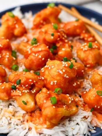 A close-up of a plate full of white rice with bang bang cauliflower served over it.