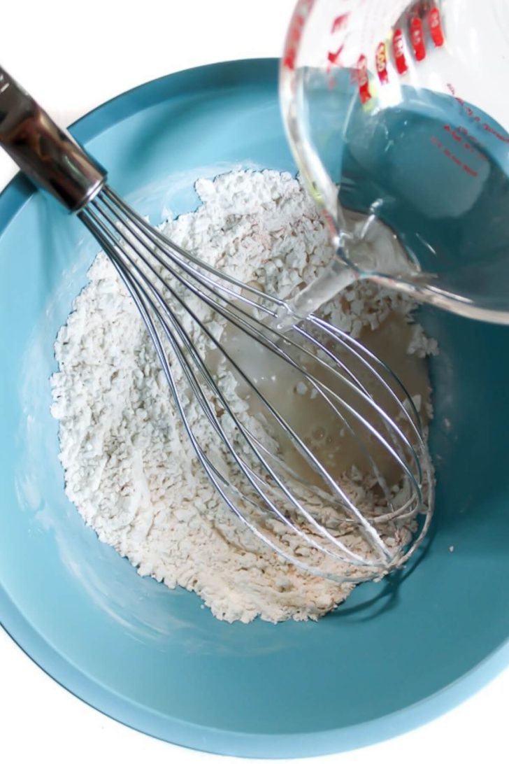 A blue bowl with dry ingredients with someone poring water into it.