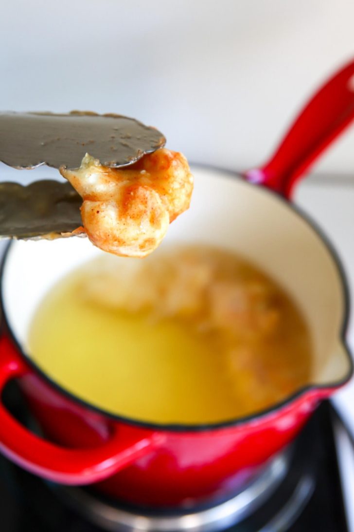 Battered deep-fried cauliflower being taken out of oil with tongs.