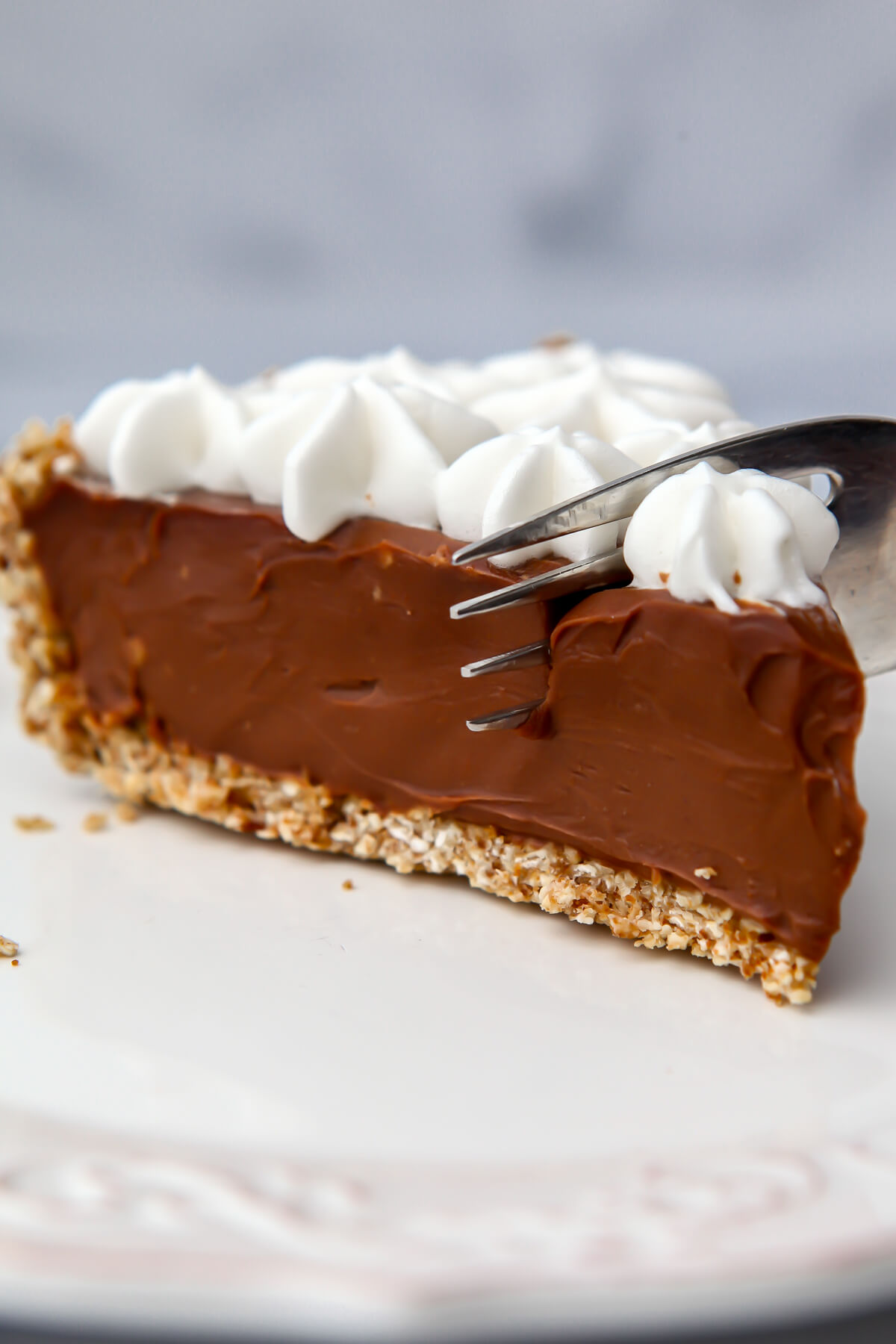 A slice of a vegan chocolate pie with vegan whipped cream on top with a fork cutting into it.