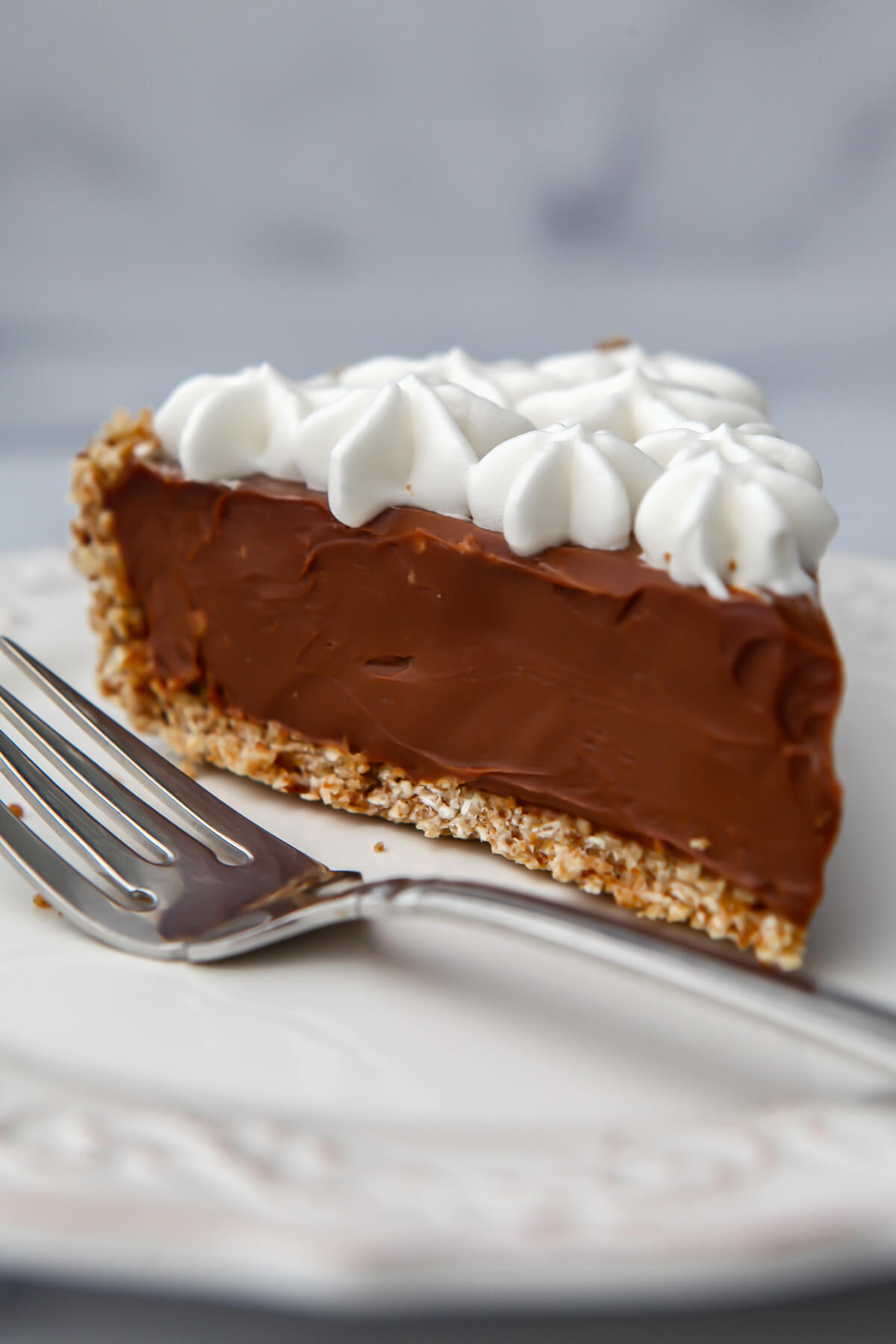 A slice of vegan chocolate cream pie on a white plate topped with vegan whipped cream.