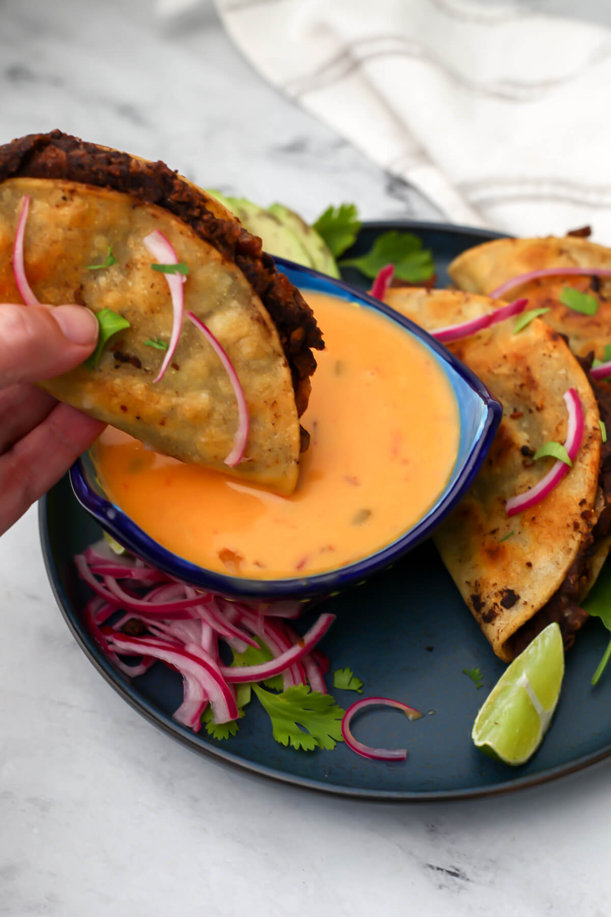 A black bean taco being dipped in vegan queso dip.