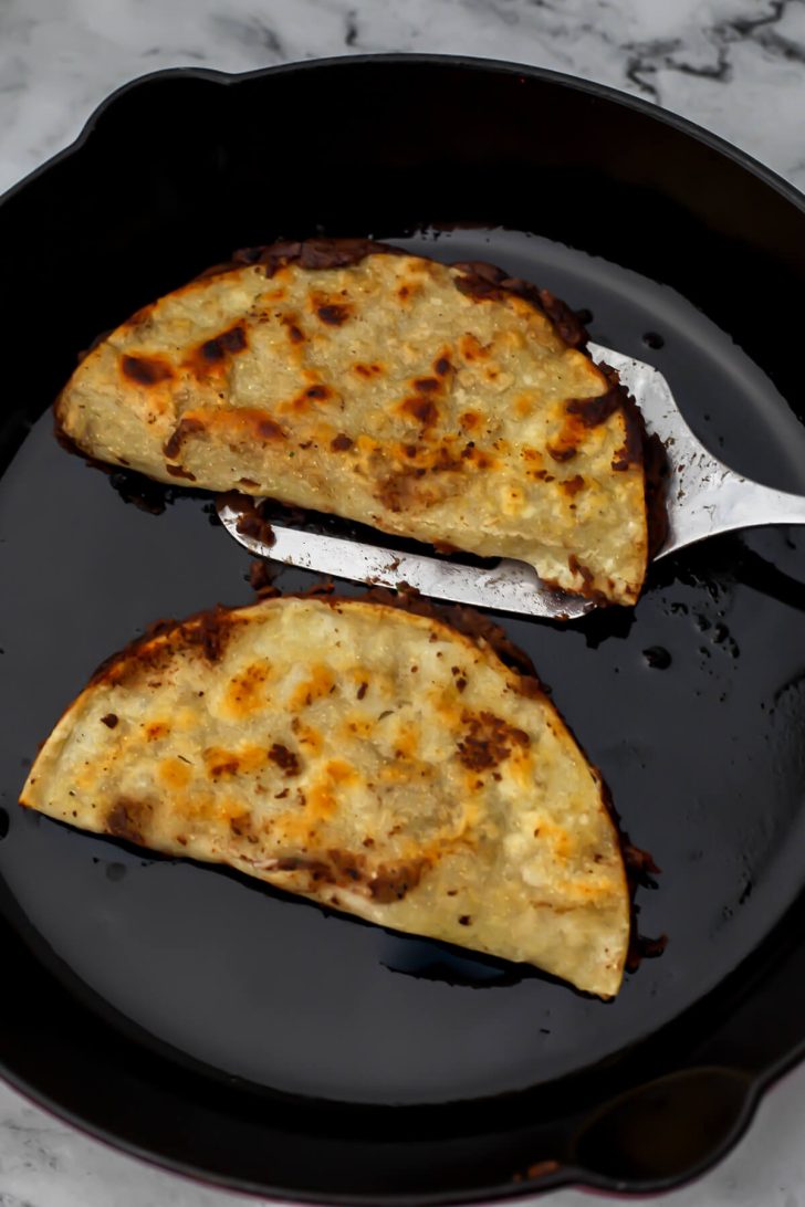 Black bean taco being fried in a hot oiled skillet to heat and crisp them up.
