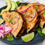 Three vegan black bean tacos on a blue plate with pickled red onions, cilantro, and lime wedges.