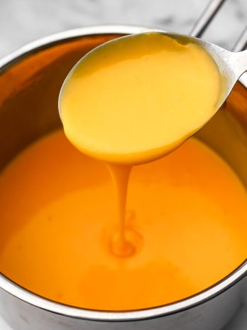 An easy vegan cheese sauce in a sauce pan with a large spoon scooping some out.