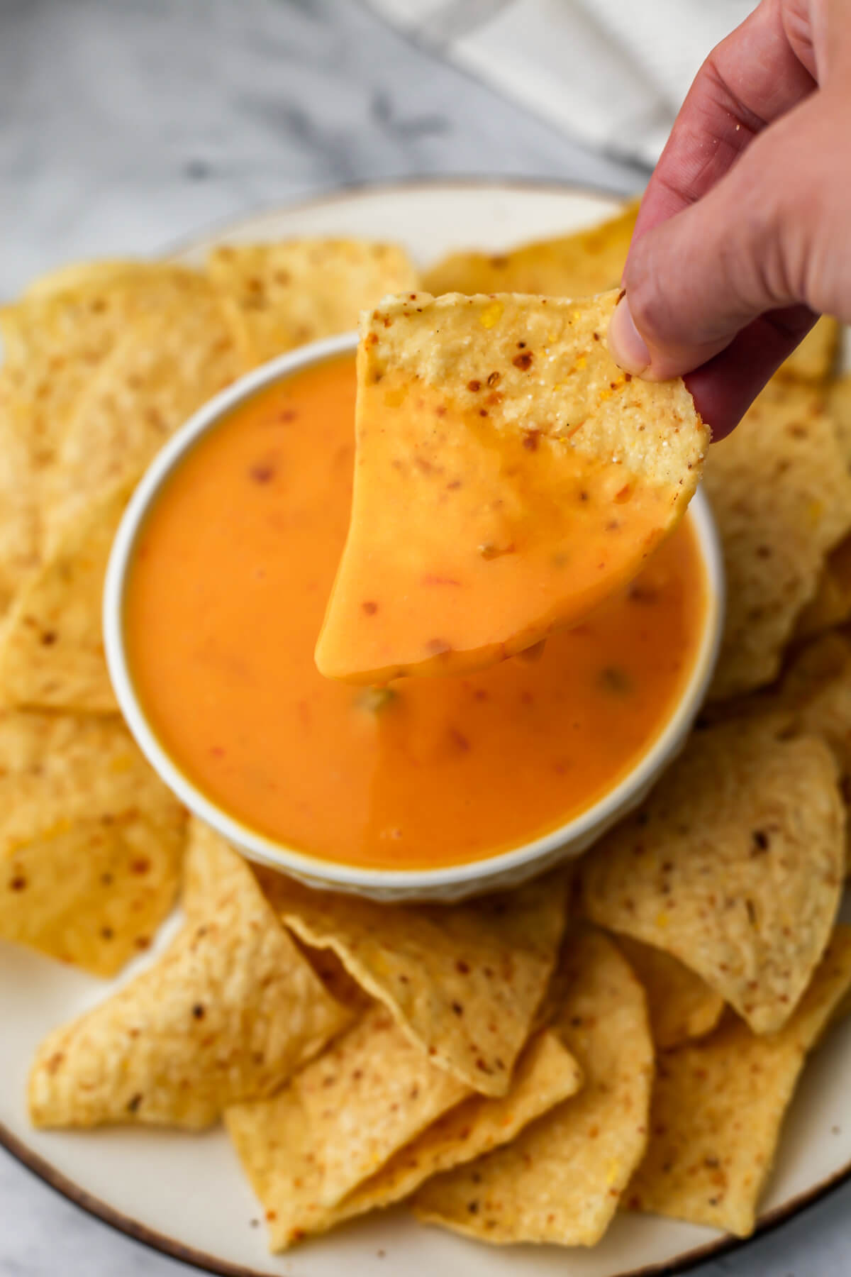 A corn chip being dipped into a bow of vegan queso cheese dip.